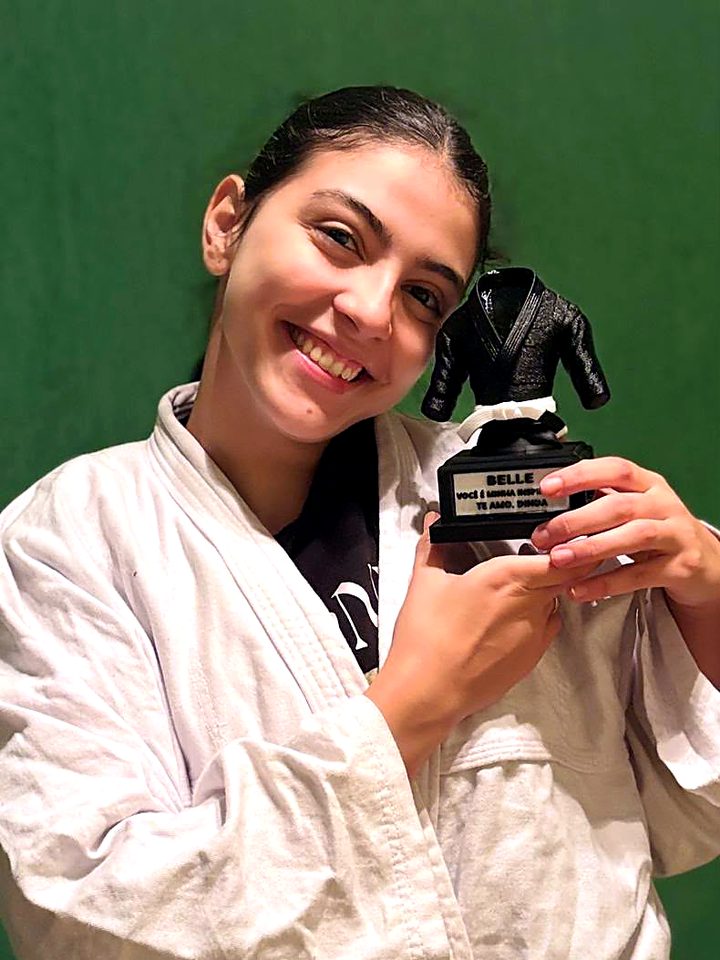 Atleta faixa branca abraçando o troféu de kimono preto